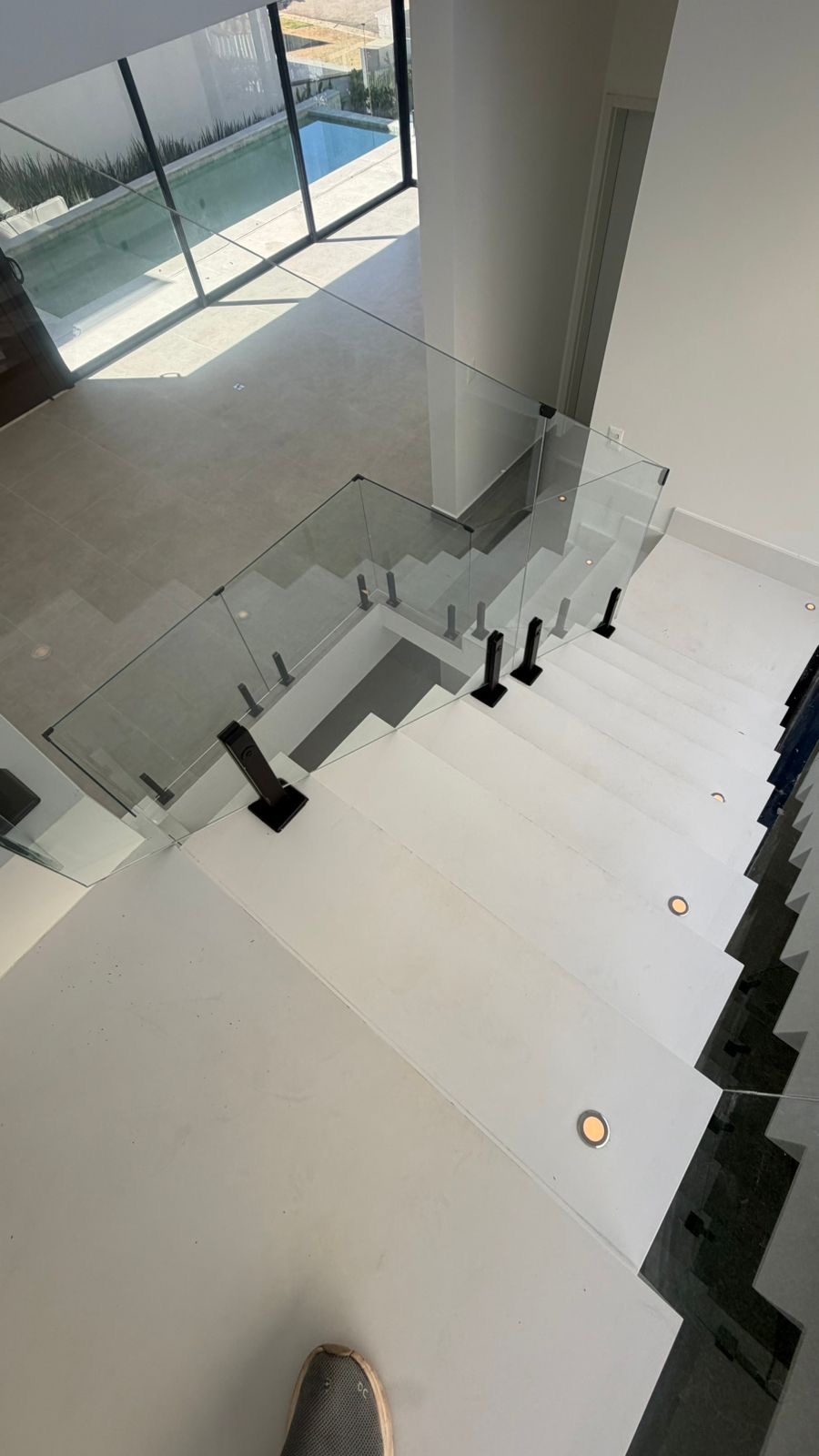 Escada em pedra com guarda-corpo de vidro para o piso superior