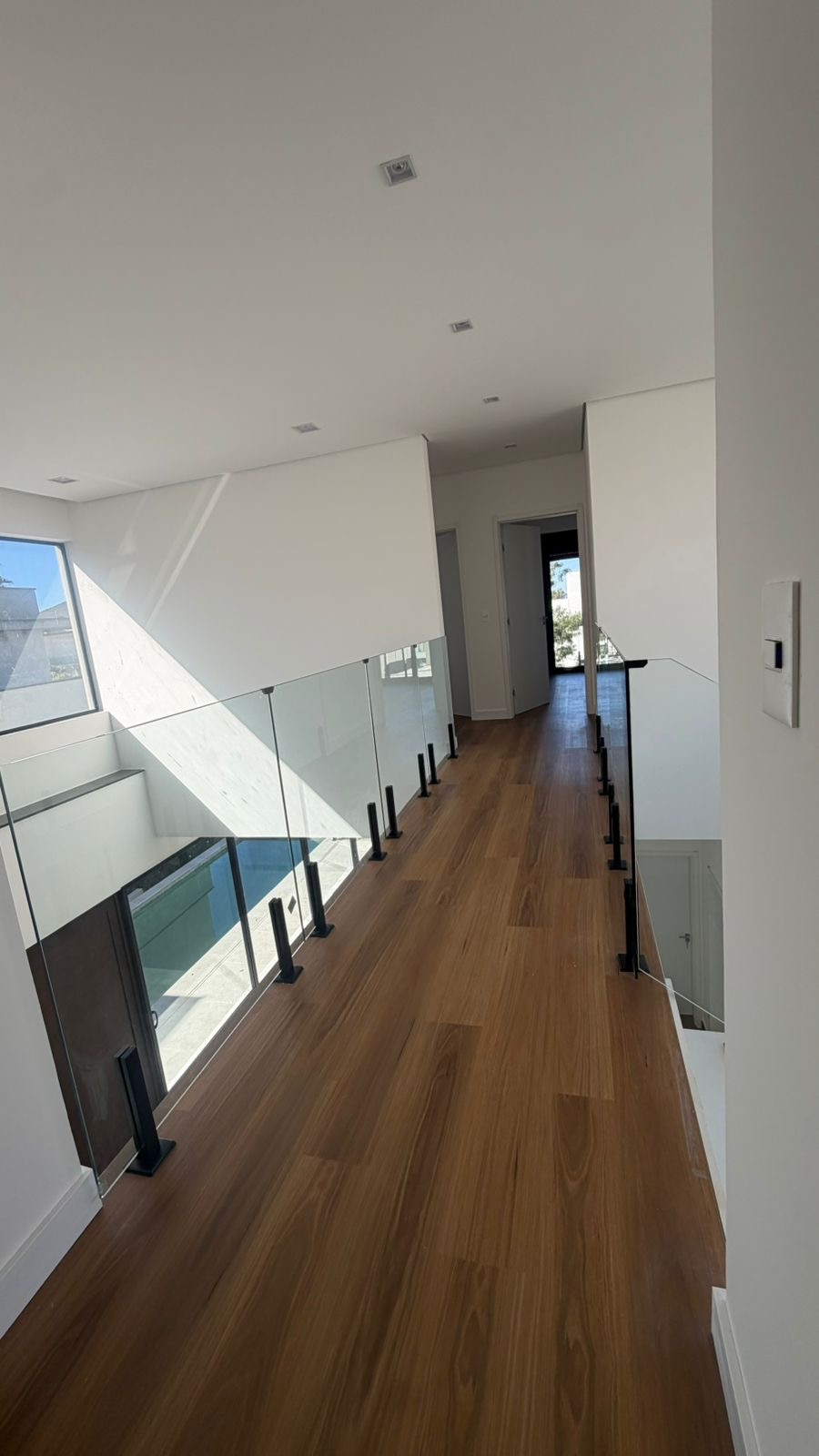 Corredor do piso superior com piso em madeira e guarda-corpo de vidro