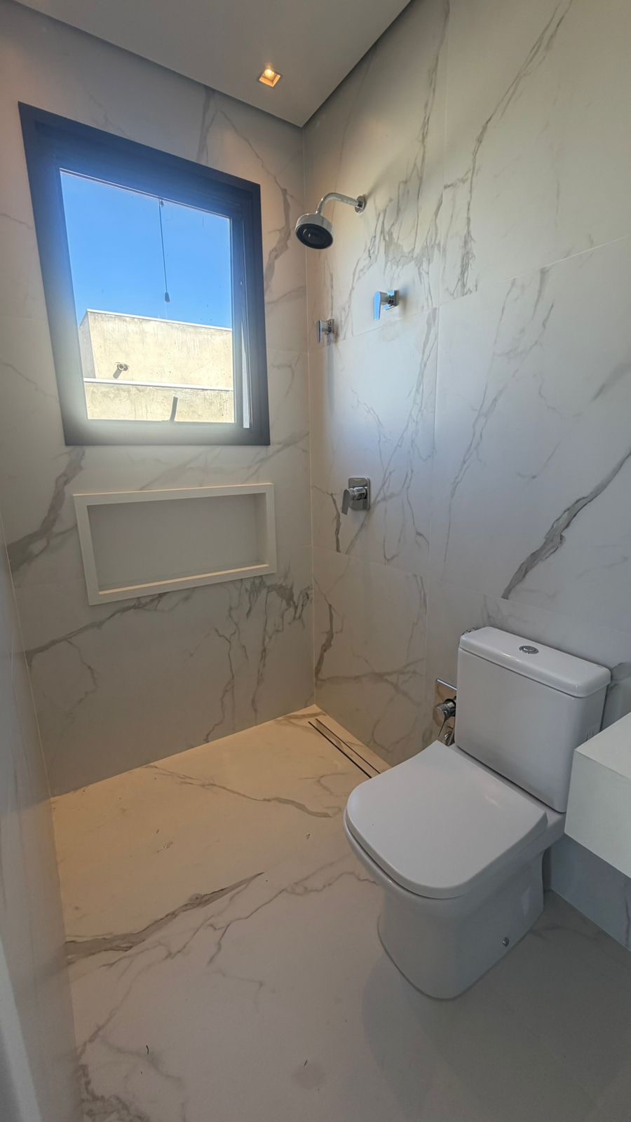 Banheiro de suíte com piso e paredes em porcelanato marmorizado